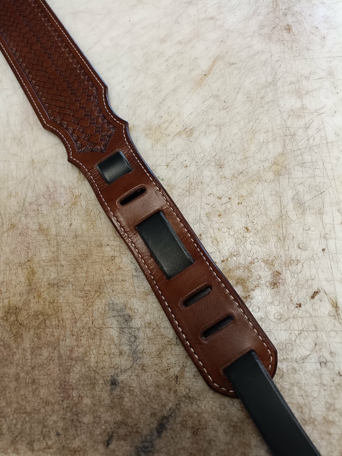 Sangle de guitare en cuir marron clair avec motif tressé Basket Weave, épaulière large et coutures blanches sur fond de cuir naturel.