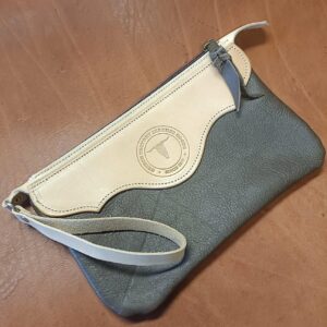 Pochette en cuir bicolore Grinch Factory Leather Goods avec logo embossé et dragonne de poignet.