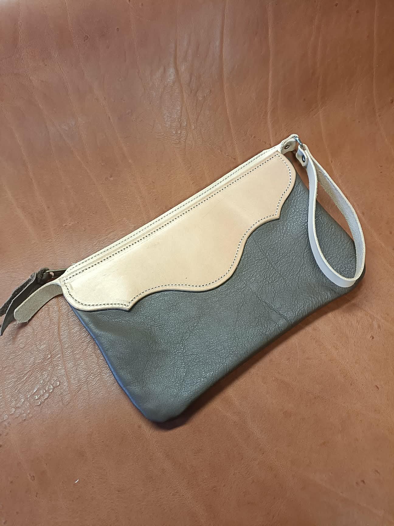 Pochette en cuir bicolore Grinch Factory Leather Goods avec logo embossé et dragonne de poignet.