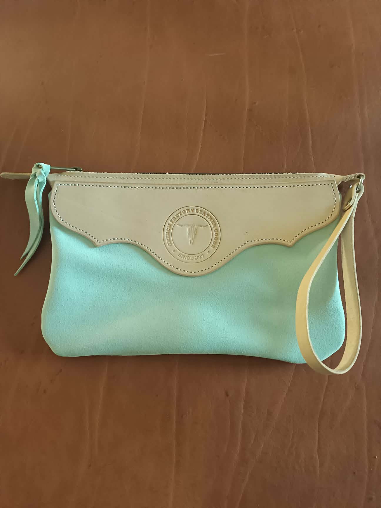 Pochette en cuir bicolore Grinch Factory Leather Goods avec logo embossé et dragonne de poignet.