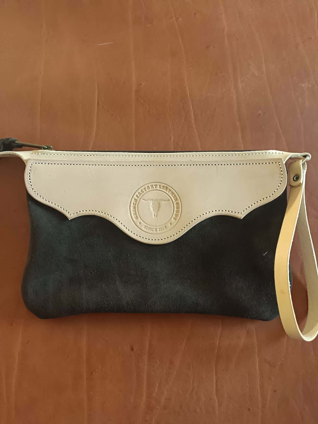 Pochette en cuir bicolore Grinch Factory Leather Goods avec logo embossé et dragonne de poignet.