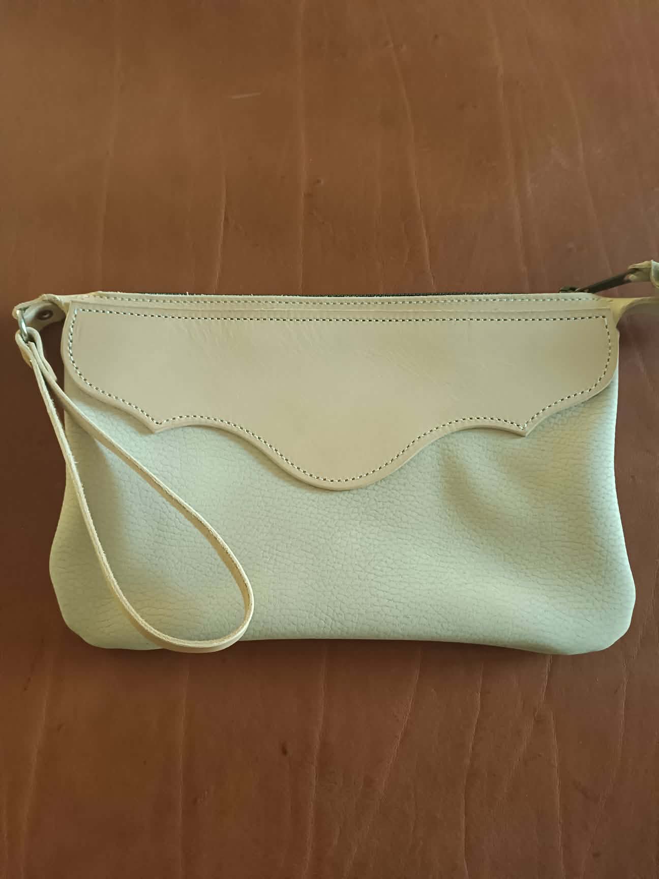 Pochette en cuir bicolore Grinch Factory Leather Goods avec logo embossé et dragonne de poignet.