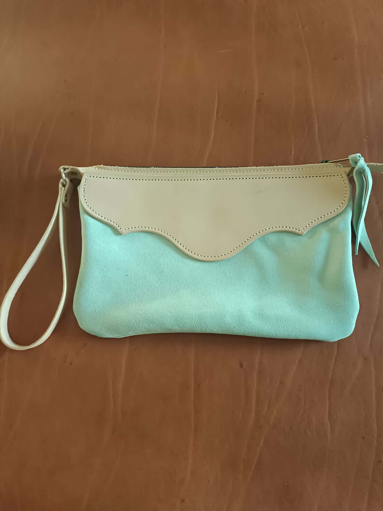 Pochette en cuir bicolore Grinch Factory Leather Goods avec logo embossé et dragonne de poignet.