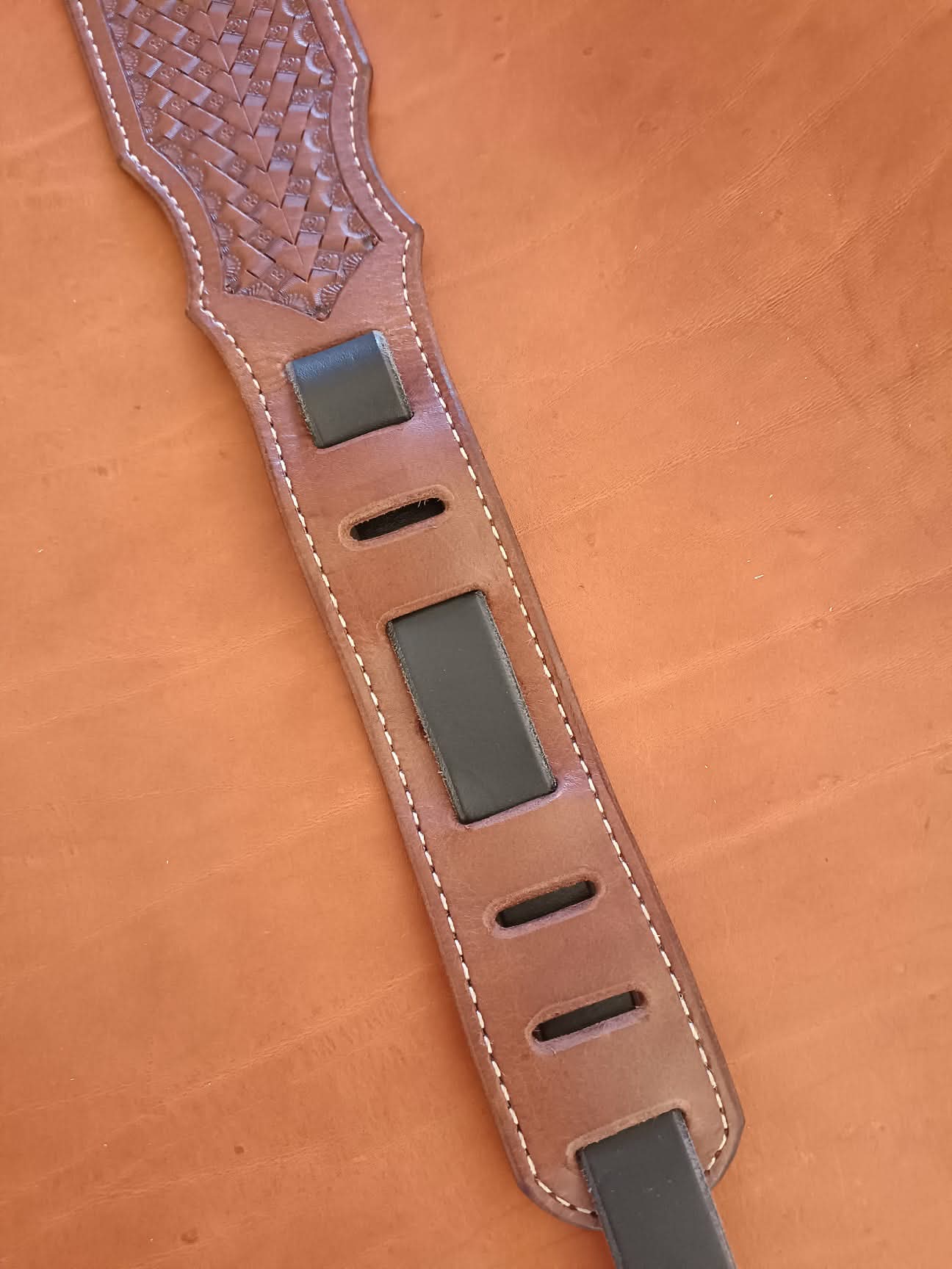 Sangle de guitare en cuir marron clair avec motif tressé Basket Weave, épaulière large et coutures blanches sur fond de cuir naturel.