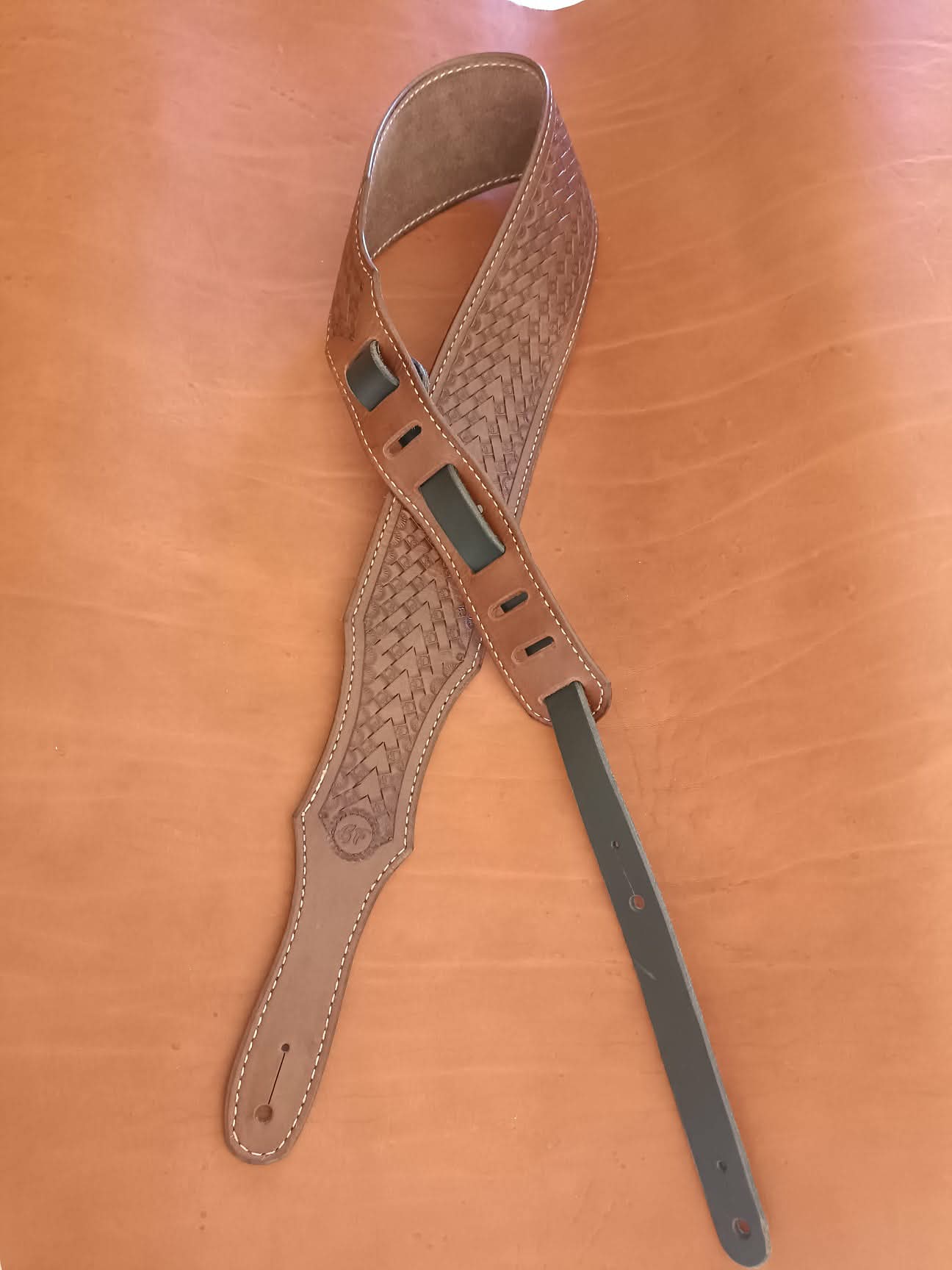 Sangle de guitare en cuir marron clair avec motif tressé Basket Weave, épaulière large et coutures blanches sur fond de cuir naturel