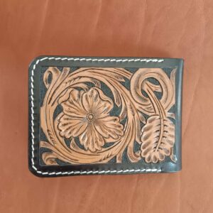 Face avant d'un portefeuille bifold en cuir noir avec motif floral brun repoussé à la main et coutures blanches.
