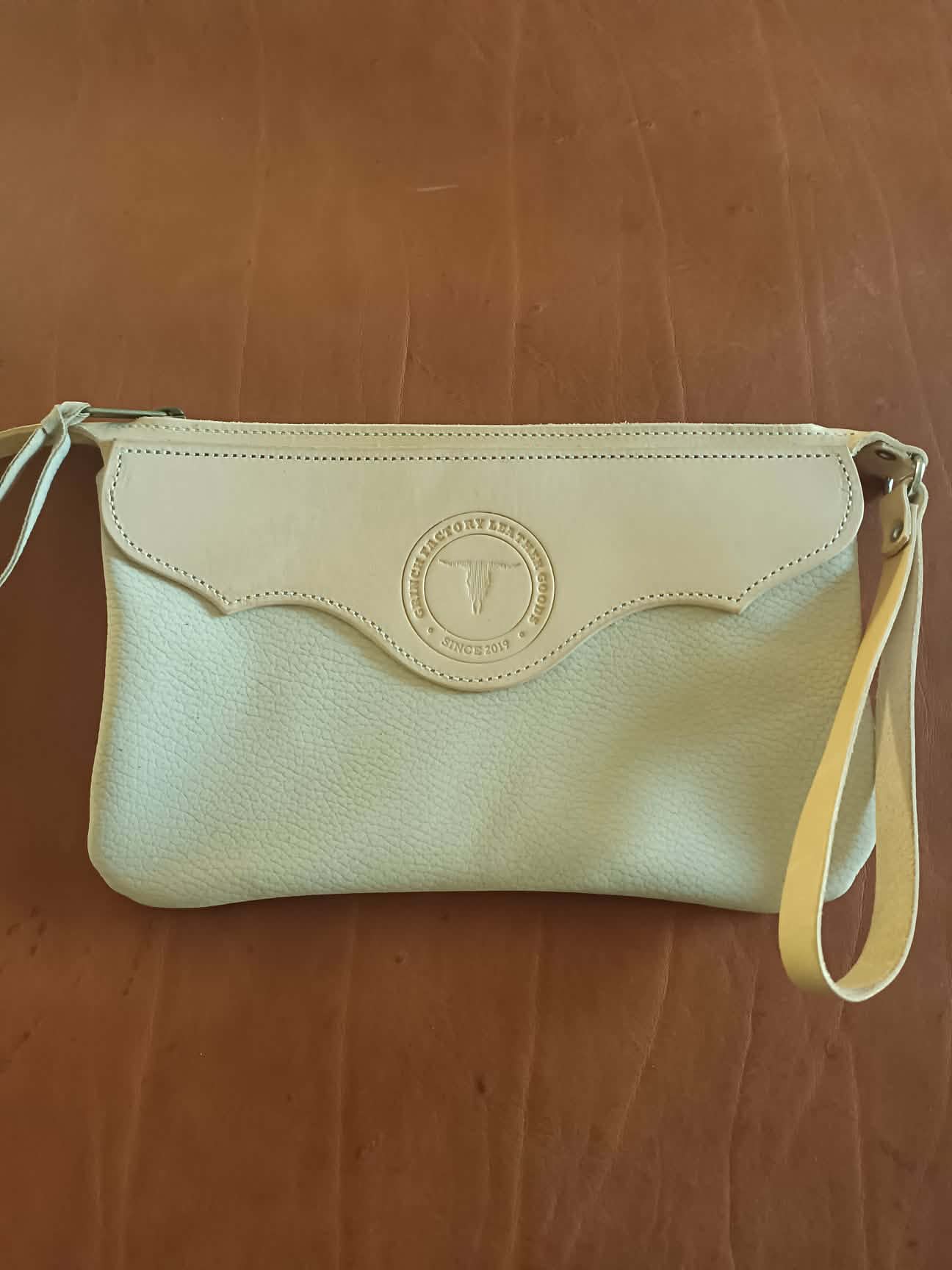 Pochette en cuir bicolore Grinch Factory Leather Goods avec logo embossé et dragonne de poignet.